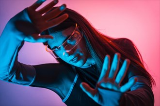 Futuristic studio portrait with neon lights of a transgender person gesturing while using smart goggles