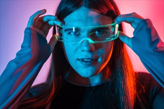 Futuristic studio portrait with neon lights of a non-binary person putting on augmented reality goggles