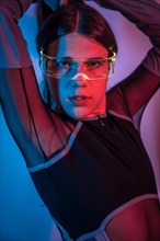 Studio portrait with neon lights of a transgender person posing sensually while using futuristic goggles