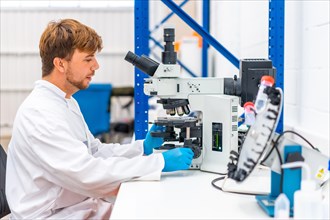 Side view of a young scientist using microscope to analyse samples in a cancer research laboratory