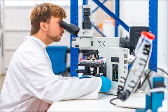 Side view of a young and caucasian scientist looking into a microscope sitting on a laboratory