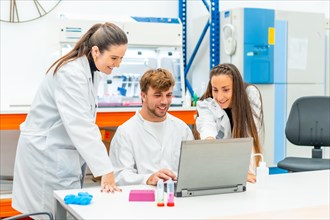 Smiling and proud young team of scientists using laptop in a research laboratory