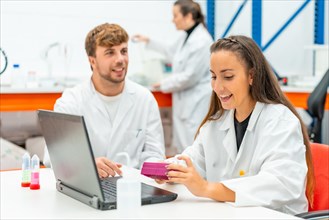 Two young and happy scientist using laptop during scholarship in the university laboratory