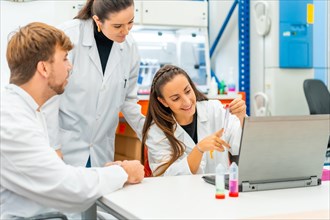 Happy female doctor using laptop while analyzing samples in a laboratory next to colleagues