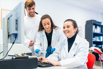 Three young doctors working in a scholarship in a laboratory using computer to analyse data