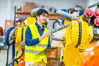 Japanese young engineer controlling the production line of robotic arms