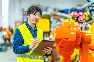 Young japanese engineer on duty controlling an industrial production line of robotic arms