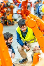 Vertical photo of two multi-ethnic young engineers reviewing the operation of robotic arms in the factory