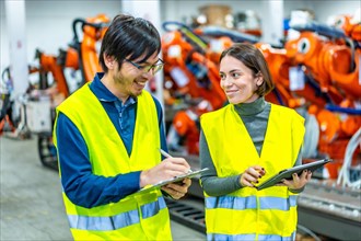 Multicultural male and female engineers smiling while controlling the assembly line of a robotic arms factory