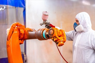 Industrial painter painting a robotic arm with spray in an industrial robot industry