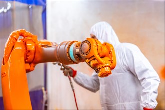 Industrial painter with protective gear painting a robotic arm with spray in an industrial robot industry