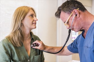 A mid-adult doctor wearing scrub clothes checking her patient's heart beat with stethoscope