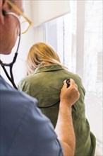 Doctor using stethoscope on his patient's back to listening to lungs for breathing problem. Vertical Shot