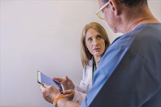 Mid-adult doctors looking at tablet while discussing a patient diagnosis. Copy space