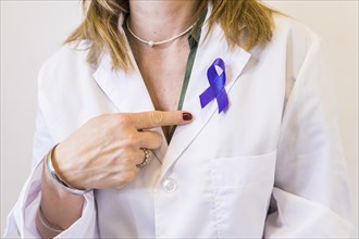 Female doctor wearing a cancer awareness ribbon while pointing at it