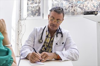 Male doctor is writing prescription to his patient at his medical office