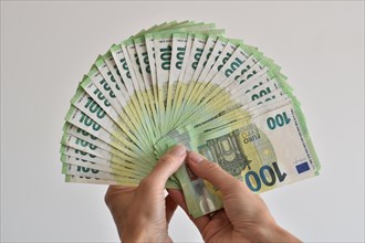 A hand counts many one hundred euro banknotes fanned out like a fan