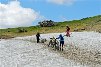 Mountain bikers pushing their mountain bike over a snow field