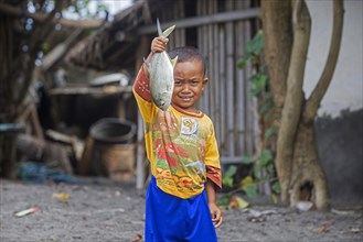 Proud Indonesian child showing caught fish in a small fishing village with bamboo houses on the island Lombok
