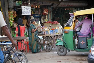 Mobile repair shop and three-wheeled taxi in busy street in Delhi