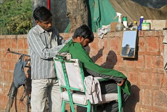 Hairdresser cutting boy's hair in the streets of Agra