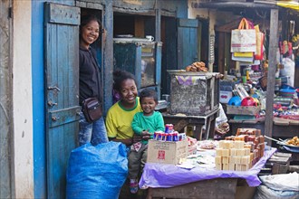 Smiling Malagasy girls with toddler in front of primitive grocery shop in the streets of the city Ambalavao
