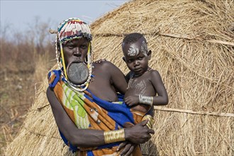 Black woman with child of the Mursi tribe wearing lip plate and beads in the Mago National Park near Jinka