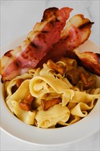 Closeup view of mushroom pasta with chanterelle and bacon on a plate