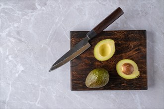 Top view of whole and halved avocado on wooden cutting board