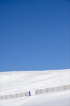 Minimalist landscape on a snowy mountain with a fence with blue sky