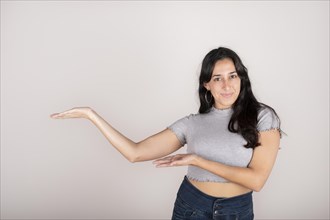 A young beautiful latin woman wearing a grey shirt over isolated white background smiling at the camera while presenting with her hands