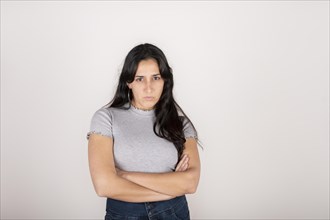 Portrait of a young latin woman dressed in a grey t-shirt with her arms crossed and an angry face