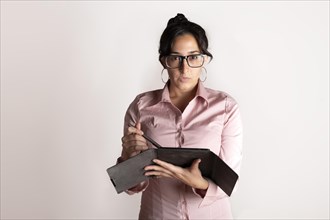 Brunette latin business woman wearing a pink shirt with a tablet in her hands on white studio background looking seriously at the camera