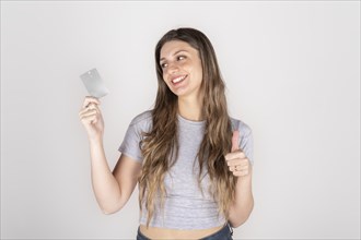 Young woman holding credit card in hand smiling with raised thumb on white studio background