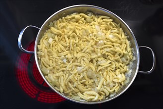 Spaetzle with onion in a pan on a red-hot hob