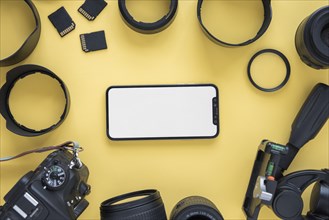 Mobile phone with blank screen surrounded by modern camera accessories yellow background