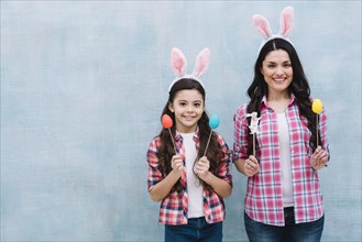 Mother daughter wearing bunny ears holding easter eggs bunny props