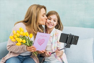 Mother with gifts kissing daughter taking selfie
