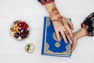 Person with mehndi holding quran near dried fruits