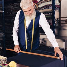 Portrait senior male fashion designer measuring fabric with wooden ruler