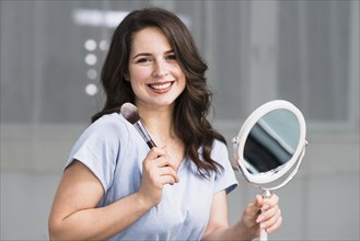 Portrait young brunette with makeup brush mirror