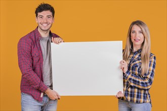 Portrait young couple presenting white placard against orange backdrop