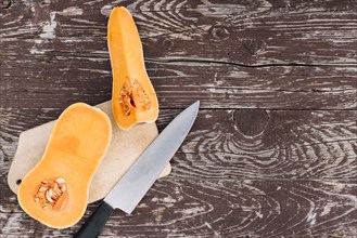 Raw orange organic butternut squash chopping board with knife wooden desk