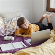 School boy sitting bed with his laptop