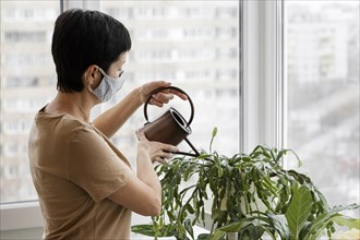 Side view woman with face mask watering indoors plants