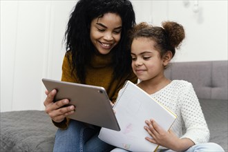 Smiley teenage girl helping sister using tablet online school