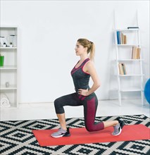 Smiling blonde young woman exercising red mat home living room