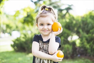 Smiling girl holding two fresh oranges park