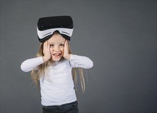 Surprised girl wearing virtual reality glasses her head touching her cheeks against gray background