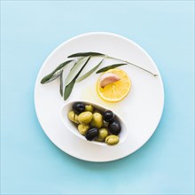 Twig lemon slice garlic clove bowl olives plate blue background